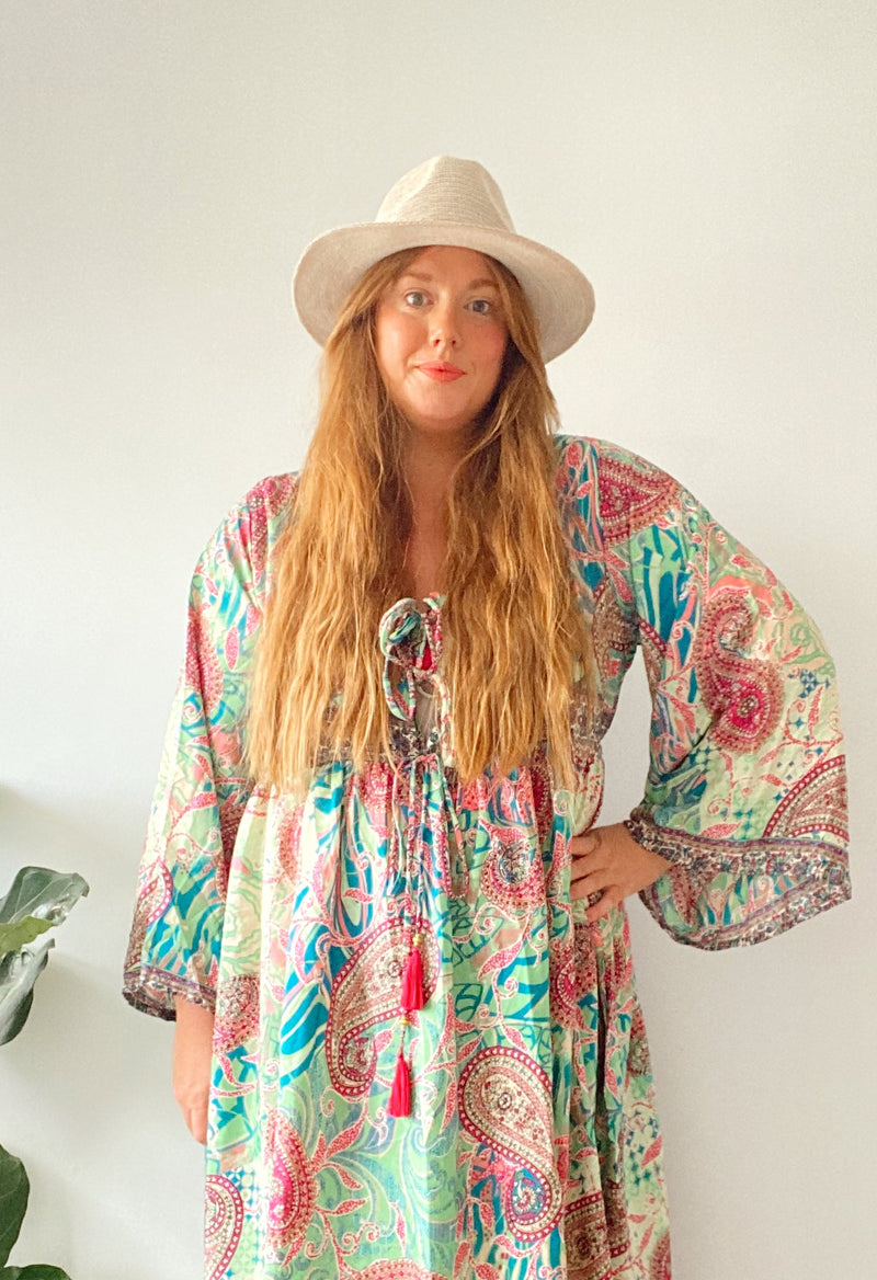 Woman wearing a colorful patterned dress and hat against a white background